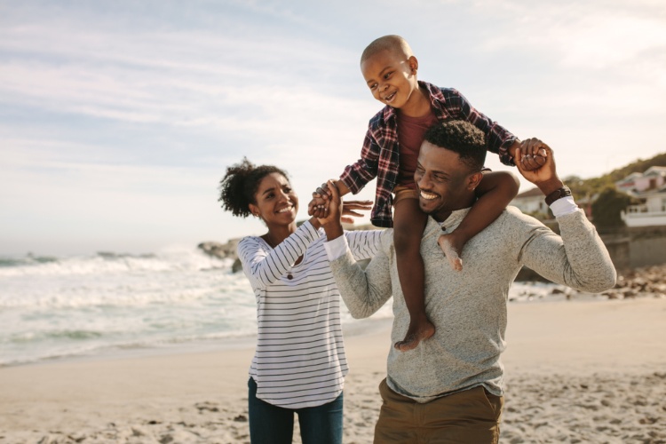 Son riding on father's shoulders on beach while mother holds his hand