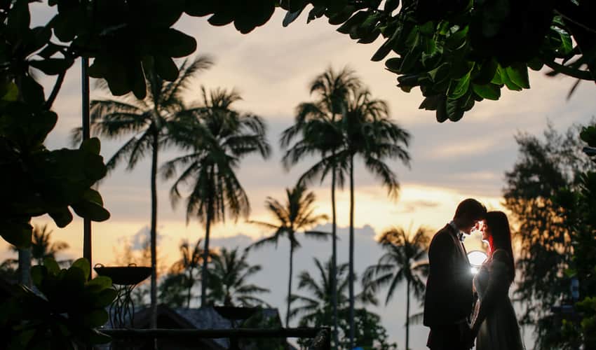 A couple taking wedding photos at sunset among palm trees