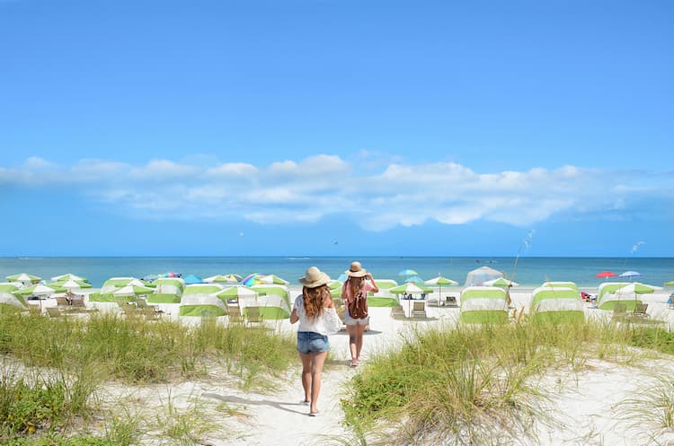 Girls walking on the beach on summer vacation. Beach chairs and parasols on beautiful white sand in the background. 