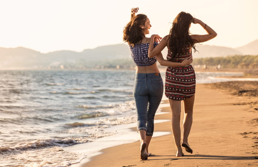 two women walk on a beach with their arms around each other