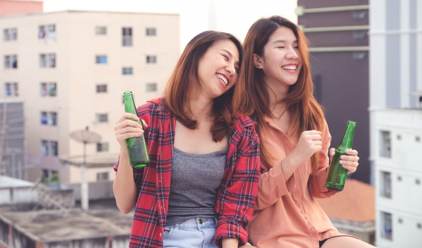 two women laugh and drink beers in a relaxed bar setting