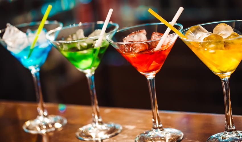 a lineup of rainbow-colored cocktails on a bartop