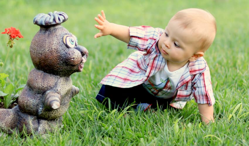 a baby plays with a caterpillar figurine on a lawn