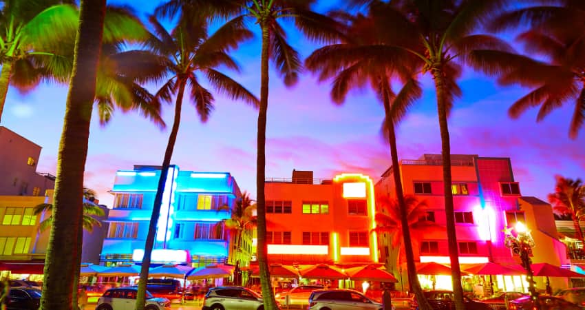 The Art Deco Historic District at sunset, neon signs of a vairety of colors illuminating the palm trees on the beach