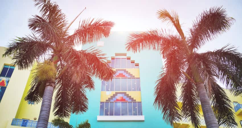 The exterior of a blue and yellow Art Deco building with palm trees 