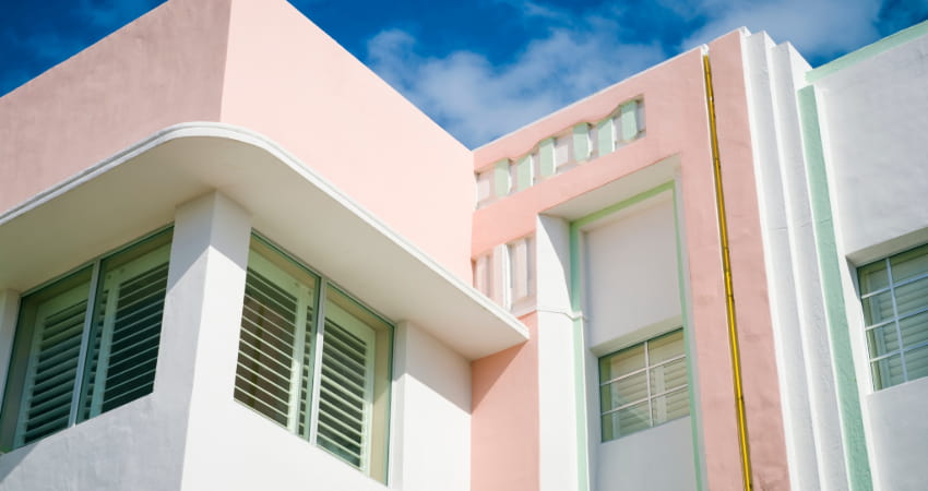 The exterior of an Art-Deco-era hotel painted white, pastel pink, and mint green