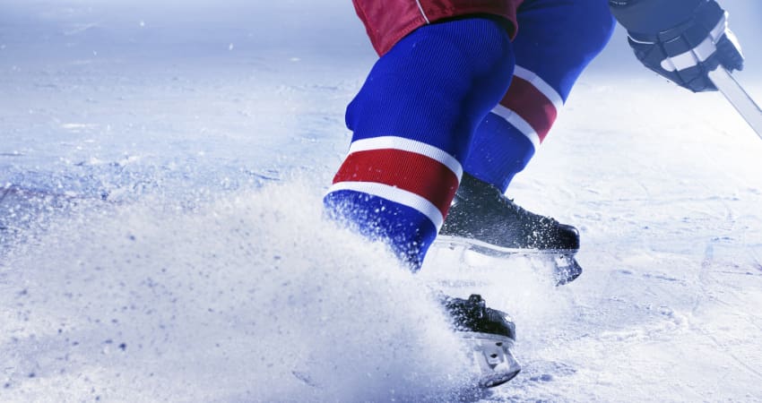 Closeup image of a hockey player turning sharply on an ice rink, kicking up shreds of ice