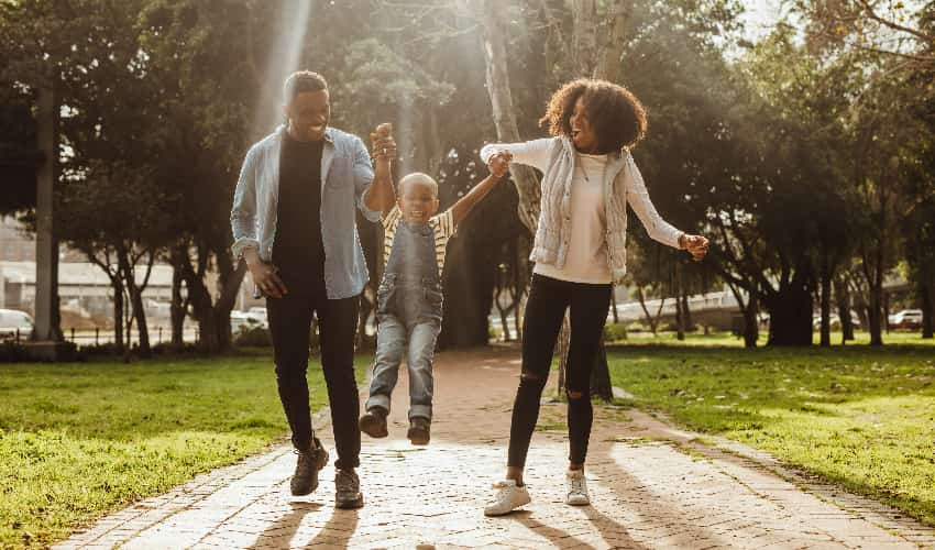 A family laughs and walks through a green and sunny park