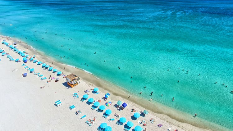 crystal blue water against a sandy shoreline with chairs and umbrellas across the beach