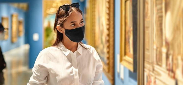 a woman wearing a mask looks at a painting in an art museum