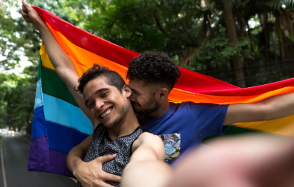 two men embrace and hold up a rainbow flag at a Pride parade