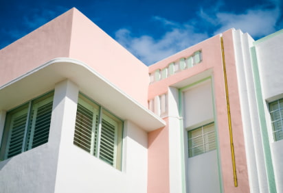 The exterior of an Art-Deco-era hotel painted white, pastel pink, and mint green