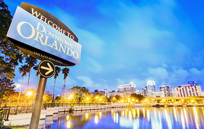 A sign in front of Lake Eola Park reads "Welcome to Orlando" with the city skyline in the background