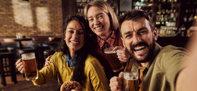 friends smile for the camera and hold up their beers