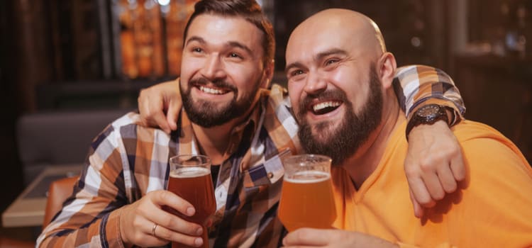 two friends hold beers and smile at a brewery